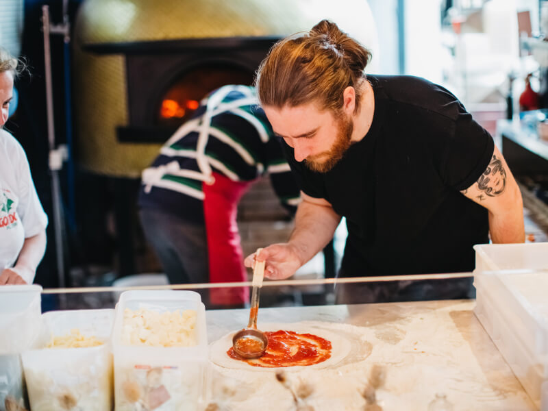 A man is making a pizza by adding sauce to a base.